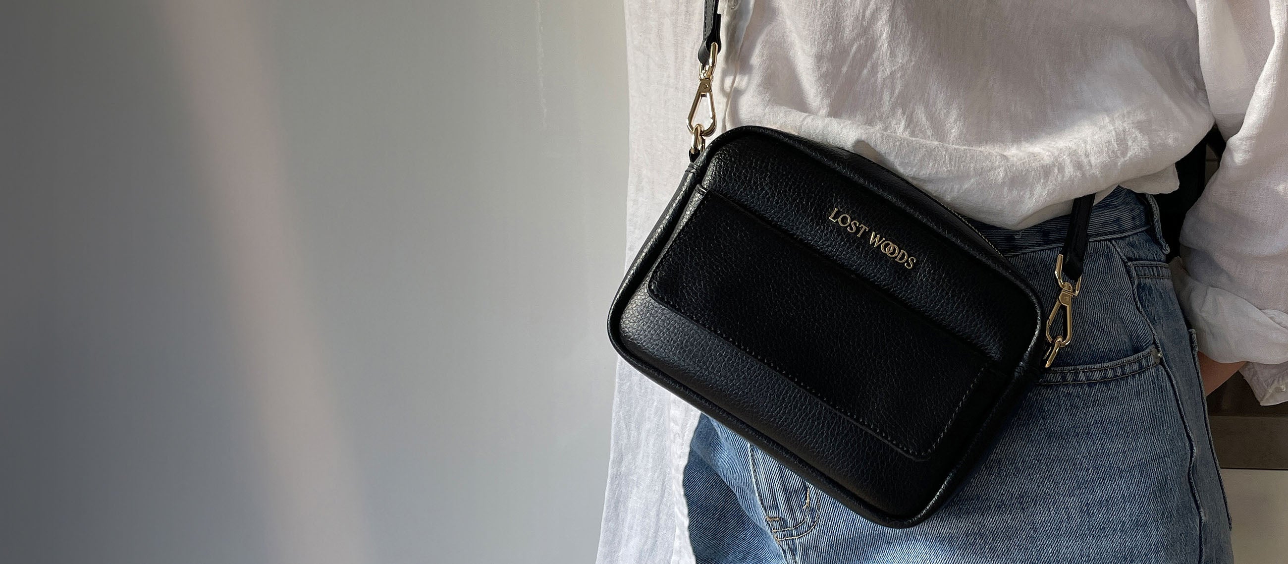 Close up of Lost Woods Aster vegan crossbody bag - made from Natural Fiber Welding's MIRUM leather alternative. The plant-based leather is black, with a pebbled grain. It has glistening gold hardware with a Lost Woods logo plate.